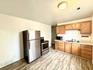 Kitchen featuring appliances with stainless steel finishes, light wood-style floors, light countertops, a sink, and baseboards