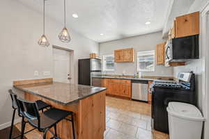 Kitchen featuring stainless steel appliances, a peninsula, a sink, a textured ceiling, and a kitchen bar