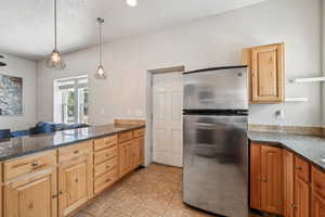 Kitchen featuring freestanding refrigerator, decorative light fixtures, dark stone counters, light tile patterned floors, and a peninsula