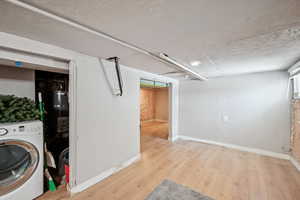 Finished below grade area featuring washer / dryer, wood finished floors, strapped water heater, and baseboards