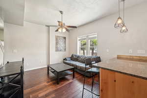 Living area featuring a ceiling fan, dark wood-style floors, a textured ceiling, and baseboards