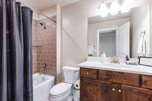 Bathroom featuring toilet, shower / bathtub combination with curtain, and vanity