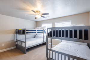 Carpeted bedroom with multiple windows, ceiling fan, and baseboards