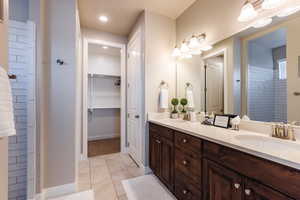 Full bathroom featuring double vanity, tile patterned flooring, a spacious closet, baseboards, and tiled shower