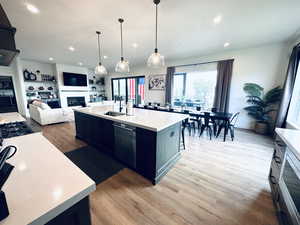 Kitchen with a fireplace, dishwashing machine, a sink, light countertops, and light wood-style floors