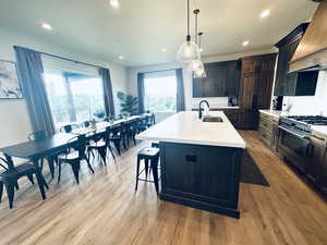 Kitchen with a sink, stainless steel stove, custom exhaust hood, a kitchen island with sink, and light countertops