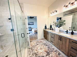 Bathroom featuring a stall shower, ensuite bath, double vanity, ceiling fan, and baseboards
