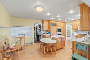 Kitchen with a center island, white appliances, light countertops, light wood-type flooring, and a breakfast bar area