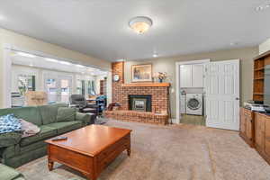 Living area featuring separate washer and dryer, a brick fireplace, carpet, french doors, and baseboards