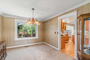 Unfurnished dining area with wallpapered walls, a chandelier, light colored carpet, and crown molding