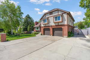 English style home with stucco siding, brick siding, concrete driveway, a garage, and a gate