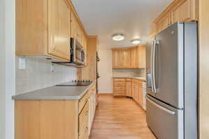 Kitchen with stainless steel appliances, light brown cabinets, light wood finished floors, light countertops, and backsplash