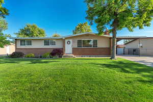 Ranch-style house with brick siding, a chimney, a carport, driveway, and a gate