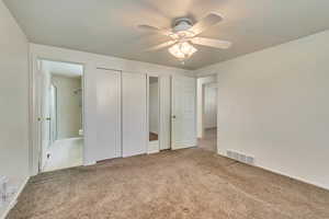 Unfurnished Primary bedroom featuring carpet flooring, ceiling fan, closets and ensuite bath