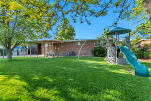 Back of property featuring brick siding, a playground, a lawn, and a patio