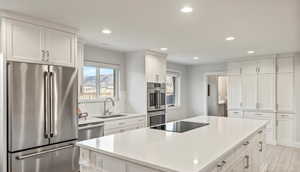 Kitchen featuring appliances with stainless steel finishes, a sink, recessed lighting, white cabinets, and a kitchen island