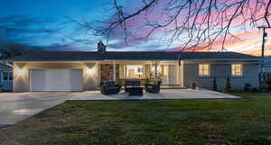 Rear view of house with outdoor lounge area, concrete driveway, a lawn, an attached garage, and a chimney