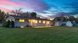 View of front facade with a shed, an outbuilding, a lawn, and brick siding
