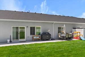 Back of property featuring a patio, roof with shingles, stucco siding, and a lawn