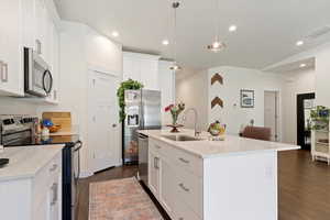 Kitchen featuring stainless steel appliances, a sink, dark wood-style flooring, white cabinets, and light countertops