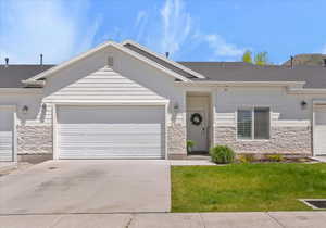 Ranch-style home featuring driveway, an attached garage, stone siding, and a front lawn