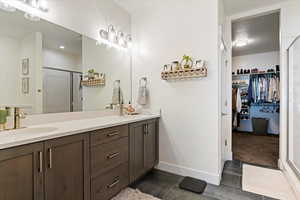 Full bathroom with a shower stall, double vanity, baseboards, wood finished floors, and a spacious closet