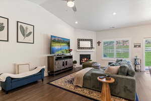 Living room featuring wood finished floors, lofted ceiling, ceiling fan, a fireplace, and recessed lighting