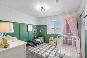 Carpeted bedroom with wainscoting, a textured ceiling, and a decorative wall