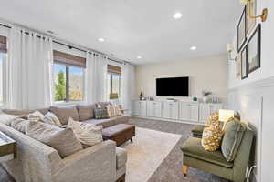 Carpeted living room with recessed lighting and custom window coverings