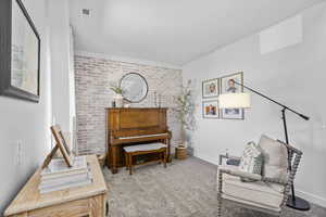 Sitting room featuring carpet flooring, brick accent wall, and baseboards