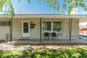 Doorway to property with a chimney, brick siding, and covered porch