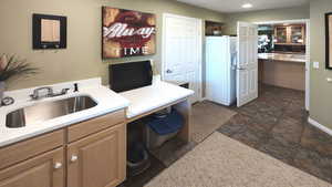 Kitchen featuring white fridge with ice dispenser, a sink, stone tile floors, an office area, and light stone counters