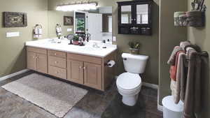Full bathroom featuring toilet, double vanity, and baseboards
