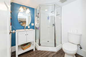 Full bathroom with wood finished floors, a shower stall, toilet, and vanity
