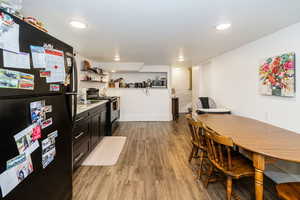 Kitchen featuring black appliances, light wood finished floors, open shelves, light countertops, and dark cabinetry