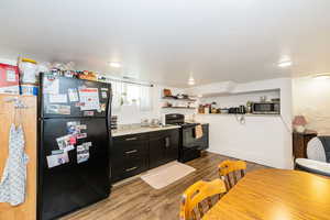 Kitchen featuring black appliances, dark cabinetry, light wood-type flooring, a sink, and open shelves
