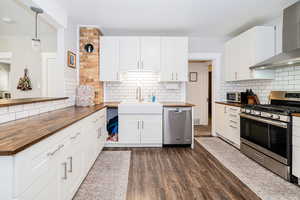 Kitchen with wood counters, appliances with stainless steel finishes, wall chimney range hood, a sink, and tasteful backsplash
