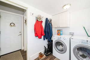 Washroom featuring dark wood-style floors, washing machine and clothes dryer, cabinet space, and baseboards