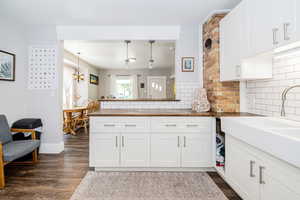 Kitchen with butcher block counters, dark wood-style flooring, decorative backsplash, white cabinets, and a peninsula