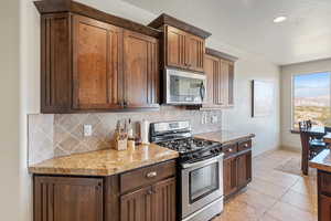 Kitchen featuring stainless steel appliances, decorative backsplash, baseboards, light tile patterned floors, and light stone counters