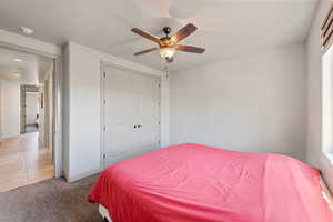Bedroom featuring a closet, light colored carpet, light tile patterned floors, a ceiling fan, and baseboards