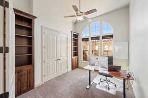 Office with a towering ceiling, carpet flooring, a ceiling fan, and built in shelves