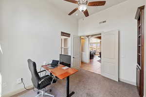 Office space featuring ceiling fan, light carpet, baseboards, light tile patterned floors, and a high ceiling