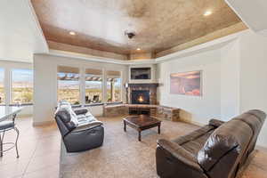 Living area with a tray ceiling, a stone fireplace, baseboards, light tile patterned floors, and recessed lighting