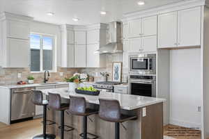Kitchen with stainless steel appliances, a center island, a breakfast bar area, light stone countertops, and light wood finished floors
