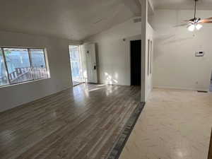 Unfurnished living room featuring lofted ceiling, healthy amount of natural light, ceiling fan, and wood finished floors