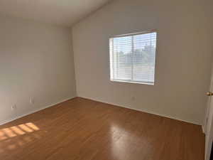 Unfurnished room with wood finished floors, lofted ceiling, and baseboards