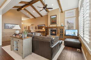 Living area featuring beamed ceiling, a tiled fireplace, light wood finished floors, a ceiling fan, and high vaulted ceiling