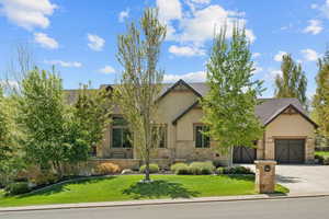 View of front facade with stone siding, concrete driveway, an attached garage, a front yard, and stucco siding