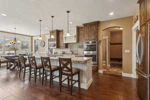 Kitchen with stainless steel appliances, arched walkways, backsplash, an island with sink, and dark wood finished floors